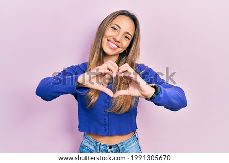 Beautiful hispanic woman wearing casual blue shirt smiling in love doing heart symbol shape with hands. romantic concept. 