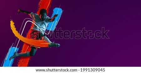 Kick in jump. Portrait of African man, male soccer football player in white red uniform isolated on purple neon background. Concept of active life, team game, energy, sport. Copy space for ad.