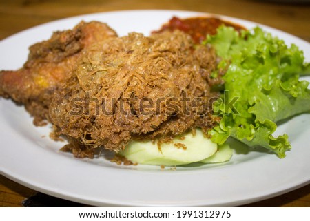 fried chicken omelet with cucumber slices and green leafy vegetables on a plate on a wooden table for dinner called Pecel Ayam