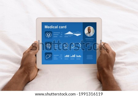 Male hands holding digital tablet with information from medical card on screen, top view, closeup. Black man reading info about his medical condition and anamnesis online, using mobile app on pad