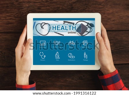 Cropped of young man using online health application on digital tablet over wooden background, closeup, top view. Male hands holding pad, making online appointment with his physician