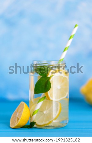 Tasty cool beverage with lemon and basil in mason jar glass on blue background