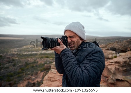 Portrait of young male hiker taking photos of mountains and beautiful sunrise with professional camera