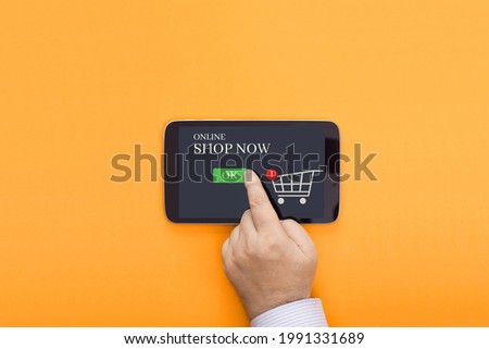 Conceptual photo representing online shopping. A finger presses on the screen of a mobile device to make a purchase.