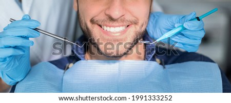Unrecognizable male patient having teeth whitening procedure at modern dental clinic, smiling at camera, dentist hands in rubber gloves with dental tools. Banner for dental clinic, panorama