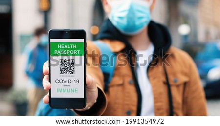 Close up portrait view of short haired serious man calmly looking at camera and showing vaccine passport at his smartphone while standing at the empty street during the coronavirus pandemic Royalty-Free Stock Photo #1991354972