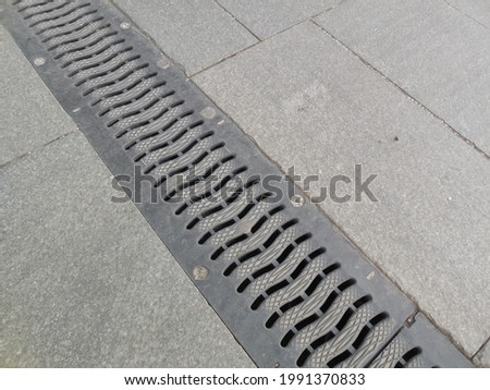 The metal grid of the drainage tray (storm sewer) on the street is paved with gray paving slabs.