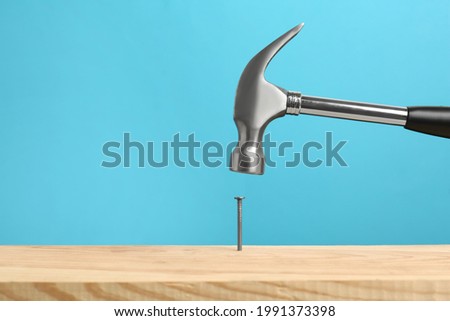 Hammering nail into wooden surface against light blue background Royalty-Free Stock Photo #1991373398