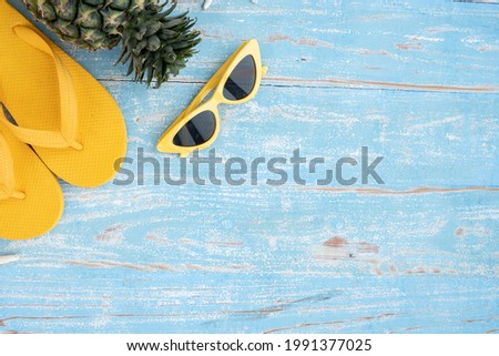 top view of yellow slippers pineapple and sunglasses on blue wooden background,Flat lay of summer and travel equipment with copy space,Summer vacation and travel concept