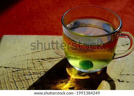 Fully linden tea filled glass pot existing on wooden plate and red carpet with black shadow background. Isolated linden tea cup made of glass and there is green mentholated sweat and candy. 