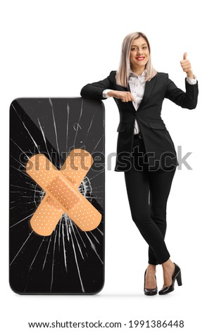 Full length portrait of a businesswoman leaning on a cracked smartphone with bandage and showing thumbs up isolated on white background