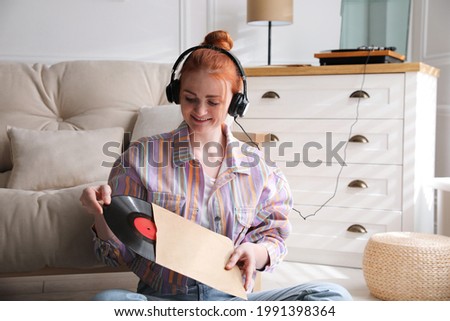 Young woman listening to music with turntable in living room Royalty-Free Stock Photo #1991398364