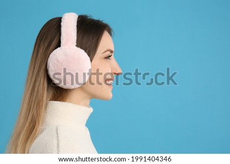 Happy woman wearing warm earmuffs on light blue background, space for text Royalty-Free Stock Photo #1991404346