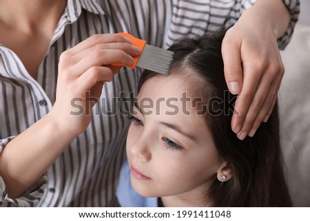 Mother using nit comb on her daughter's hair indoors. Anti lice treatment