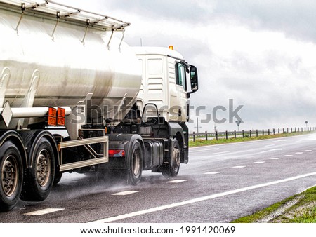 A white semitrailer tractor with a stainless tanker truck transports dangerous goods on the road. Kotsnet transportation of engine oil and diesel fuel to filling stations.  Royalty-Free Stock Photo #1991420069
