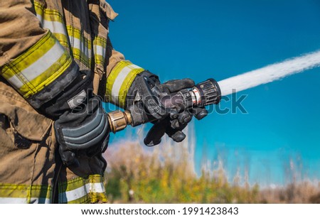 Hands of firefighter, no face, holding a hose by throwing water at high pressure.