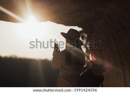 Young female tourist with backpack taking picture of the beautiful landscape in the mountain. Sun rays.