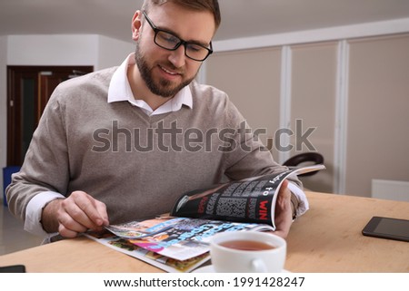 Young man reading sports magazine at table indoors