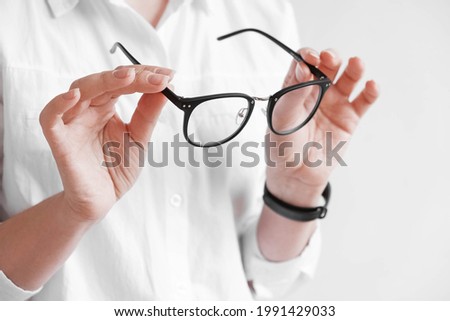 Woman holding optical glasses in a black frame on a white background. Copy, empty space