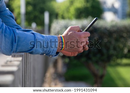Man with gay flag bracelet holding a smart phone