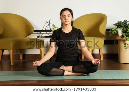 Young attractive smiling woman practicing yoga, wearing sportswear, pants and top, indoor full length at home Royalty-Free Stock Photo #1991433833