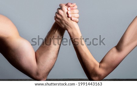  Arm wrestling thin hand and a big strong arm in studio. Two man's hands clasped arm wrestling, strong and weak, unequal match.
