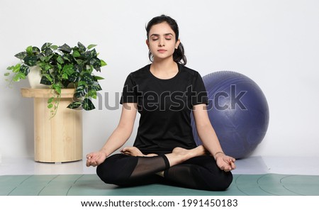 Young attractive smiling woman practicing yoga, wearing sportswear, pants and top, indoor full length at home Royalty-Free Stock Photo #1991450183