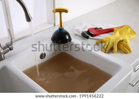 Kitchen counter with clogged sink, plunger and plumber's accessories Royalty-Free Stock Photo #1991456222