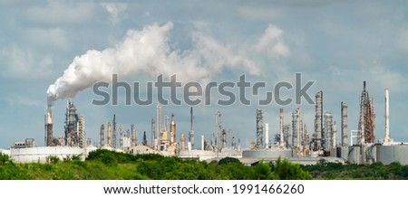 green trees in front of dirty petrochemical factory or oil refinery polluting carbon and pollution into the cloudy smog skies cuasing climate change and global warming and extreme weather events  Royalty-Free Stock Photo #1991466260