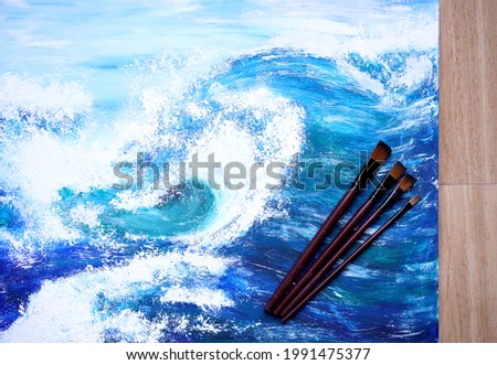Painter paint acrylic on canvas with brush with blue ocean on frame. Artwork as hobby or occupation for artist. Big wave in sea creates artwork by mix color and decors picture as hard copy art.