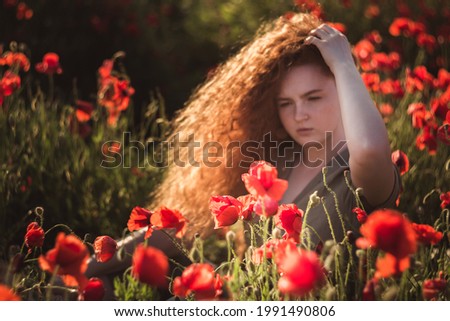 Young beautiful red-hear girl in red poppy field on sunset