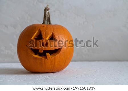 Close-up view of Halloween pumpkin with carved Jack O' Lantern face. Orange pumpkin stands on white table. Selective focus. Side view. Copy space for your text. Homemade Halloween decoration theme.
