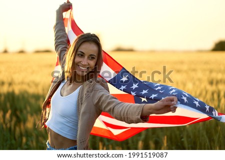 Young happy woman waving USA stars and stripes flag in golden sunset sunshine field