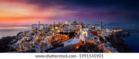 Wide panoramic view to the picturesque village of Oia on the island of Santorini, Greece, just after a summer sunset with illuminated houses and red glowing sky