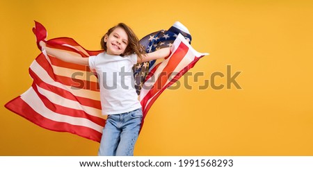 Patriotic holiday. Happy child, cute girl with American flag on yellow studio background. USA celebrate July 4th, independence Day. 