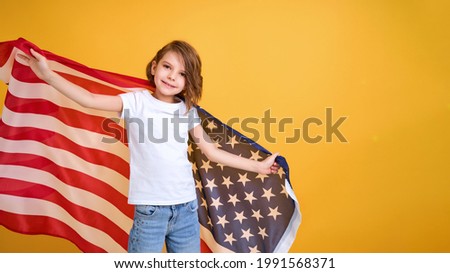 Patriotic holiday. Happy child, cute girl with American flag on yellow studio background. USA celebrate July 4th, independence Day. 