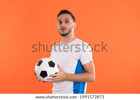 Serious looking soccer fan or player with ball isolated on colored background