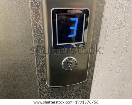 Metallic shiny chrome plated modern elevator call button with floor designation display in modern building.