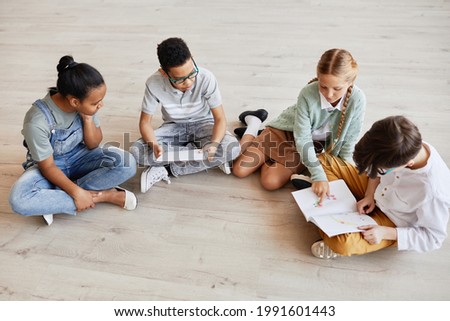 Diverse group of children sitting on floor at school and discussing pictures