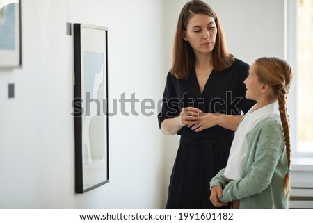 Side view portrait of mother and daughter visiting modern art gallery together and looking at pictures, copy space