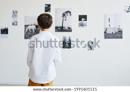Back view at young boy looking at photos in modern art gallery, copy space