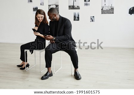 Minimal high angle portrait of elegant mixed-race couple wearing black while using smartphones in modern art gallery, copy space