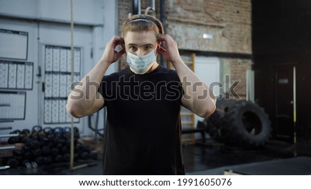 A strong athlete is putting on his face a mask and crossing his arms
