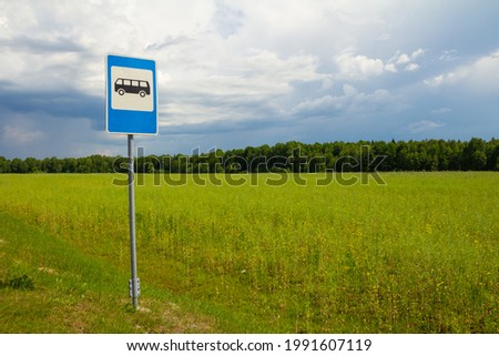 Bus stop sign on a background of blue cloudy sky, green field and forest on a summer sunny day.