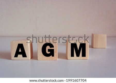 A wooden block with the word AGM Annual general meeting written on it on a white background.