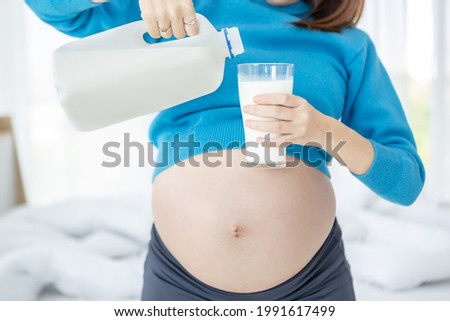 Young pregnant woman holding  milk bottle and a glass of milk in her bedroom