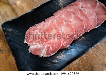 Premium dish of sliced cutlet pork or beef for BBQ meal which is served in black plate, placed on wooden table. Raw food ingredient, Top view close-up photo.