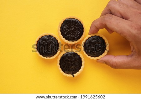 A picture of hand taking homemade chocolate tart on yellow background. Same colour subject and background concept