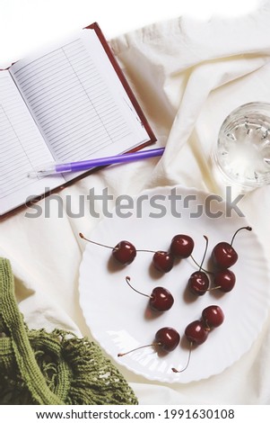 Open diary, pen, a plate of cherries and a glass of clean water. Flat lay compostion food photography