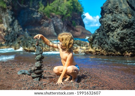Kid builds a cairn of stones on the sea coast. Beach games with children. Leisure in the evening on vacation with kids. Balance development building fantasy. Childhood. Ocean kids trawel.